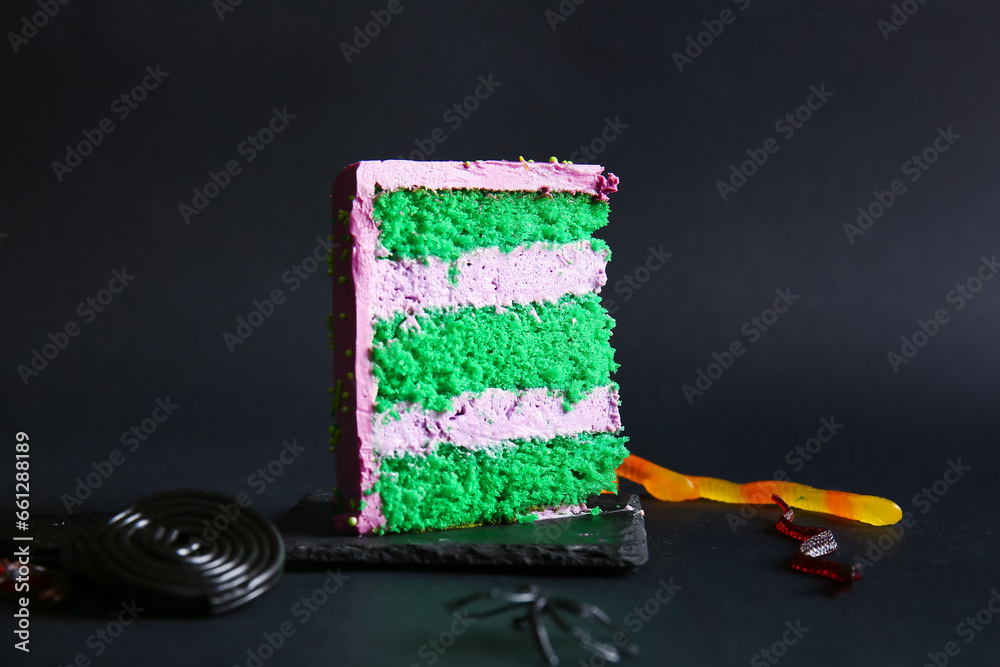 Piece of tasty Halloween cake with candy bugs on black background
