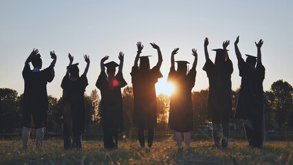 Wall Mural - College graduates in robes waving at sunset.