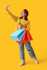 Sticker - Young woman with credit cards and shopping bags taking selfie on yellow background