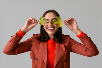 Poster - Beautiful young woman with autumn leaves on grey background