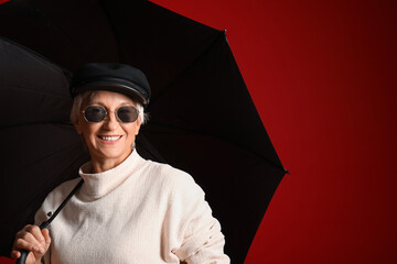 Poster - Beautiful mature woman with umbrella on red background