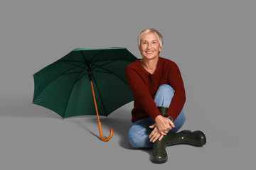 Poster - Beautiful mature woman with umbrella sitting on grey background