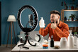 © Andrii Lysenko - Male blogger with review product talking on camera live recording video on social network at home. Online influencer selling cosmetics on social media via smartphones.