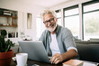 © Victor - Portrait of a relaxed senior man laughing while using his laptop at home. Modern lifestyle of the elderly people.