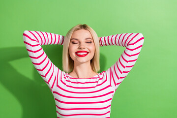 Sticker - Photo of cheerful satisfied calm woman with bob hairdo dressed striped shirt hold hands behind head isolated on green color background