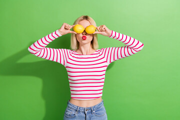 Wall Mural - Photo of pretty young girl have fun hold two fresh fruits lemons blow air summer face skincare detox isolated on green color background