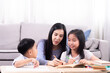 © Rakchanok - Cheerful Asian mother spend time with two sibling kids teaching homework drawing picture together in living room at home, free time children on holiday bonding happy relationship with mom parenthood