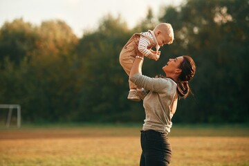 Holding kid in hands. Mother is with her little baby son are outdoors together