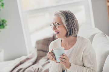 Poster - Photo of cheerful excited senior lady dressed white cardigan drinking cacao watching tv indoors house room