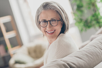 Poster - Photo of adorable pretty senior lady dressed white cardigan eyewear smiling indoors house room