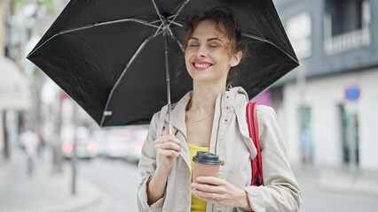 Canvas Print - Young woman holding umbrella and coffee smiling at street