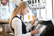Cashier, barista and young woman waitress in cafe checking for payment receipt. Hospitality, server and female butler from Canada preparing a slip at the till by a bar in coffee shop or restaurant.