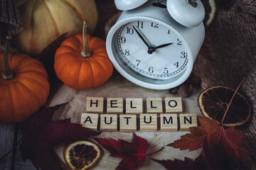 Wall Mural - Fall winter time change concept. Composition with retro alarm clock, bright yellow and red leaves, walnut. Brick wall on background. Cozy home atmosphere. Close-up. Hello Autumn message