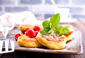 Poster - Traditional sweet syrniki or cottage cheese pancakes served with sweet cream and fresh raspberries in a white plate over table.