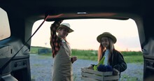 Woman gardener wearing an apron opens trunk of car her daughter puts wooden box with fresh flowers in the sunset. Mother and girl in hat harvest lavender for sale from their own field. Small family