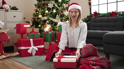 Poster - Young blonde woman upset unpacking gift sitting by christmas tree at home