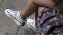 Legs Of Young Latin Woman Sitting On A Park Bench In Summertime Wearing A Short Dress And White Sneakers