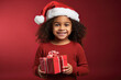 niña con gorro de papa noel sosteniendo un paquete regalo entre sus manos sobre fondo rojo