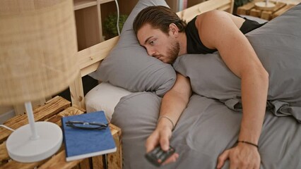 Wall Mural - Young hispanic man watching tv lying on sofa with boring expression at bedroom