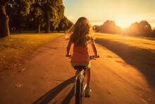 Rear View Of A Young Girl Cycling Her Bike At Sunset