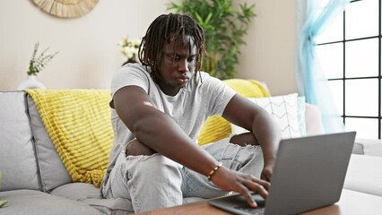 Wall Mural - African american man closing laptop lying on sofa covering face with cushion at home