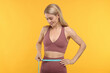 Slim woman measuring waist with tape on yellow background. Weight loss