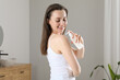 © New Africa - Happy woman applying body oil onto shoulder in bathroom