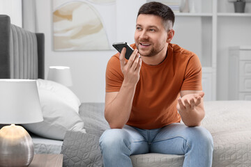 Wall Mural - Handsome man recording voice message via smartphone on bed at home