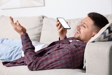 Wall Mural - Handsome man recording voice message via smartphone on sofa at home