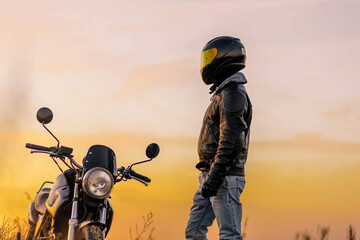 motorcyclist in a helmet and leather jacket at sunset with a classic motorcycle. Moto life concept