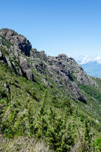 Mountainous Landscape With A Clear Blue Sky. The Mountain Is Covered In Green Vegetation And Has A Rocky Cliff Face.