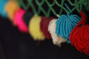 Wall Mural - Rainbow colour Yarn Tassel Garland stitched to a piece of cloth in dark shadow