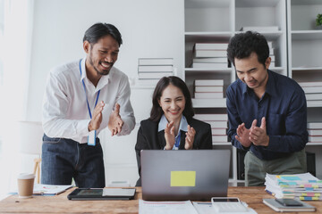 Wall Mural - Young Asian business people raising his hand to congratulate excited and happy at a successful work with laptop computer at office