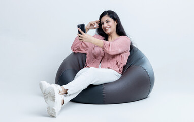 Indian latin female sitting on bean bag and talking on Video call on isolated background