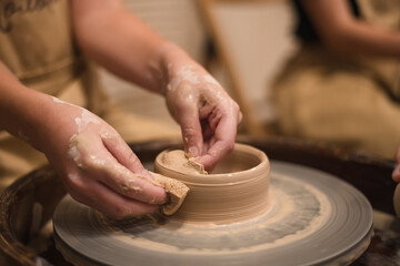 Potter girl works on potter's wheel, making ceramic pot out of clay in pottery workshop. Art and hobby concept