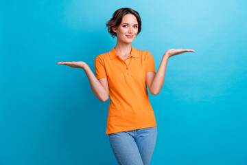 Sticker - Photo of sweet shiny girl dressed orange polo comparing arms empty space isolated blue color background