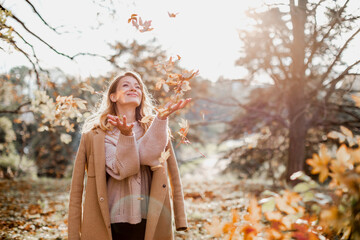 Wall Mural - Happy young woman enjoying golden autumn on a warm sunny day. Beautiful portrait of a Caucasian girl in an autumn coat walks on a warm sunny day in the autumn park. 