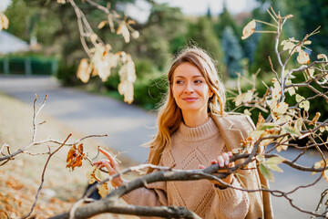 Wall Mural - Happy young woman enjoying golden autumn on a warm sunny day. Beautiful portrait of a Caucasian girl in an autumn coat walks on a warm sunny day in the autumn park.