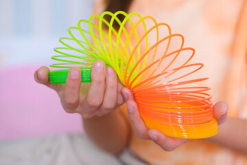 Child playing orange and green tight, colorful flexible children's toy, fun plastic toy. Teen girl plays slinky