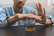 Alcoholism, depressed asian young man refuse, push out alcoholic beverage glass, drink whiskey, sitting alone at night. Treatment of alcohol addiction, having suffer abuse problem alcoholism concept.