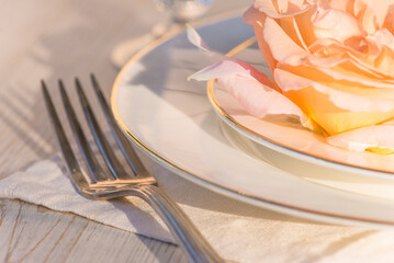 Wall Mural - Romantic table setting; close up for salmon rose flower on the white plates, fork on the white napkin son sunlight