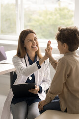 Vertical shot cheerful female pediatrician in uniform consult little boy patient at checkup meeting in clinic, celebrate good heath test result, gives high five to child. Children health-care services