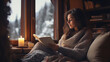 Woman sitting near window at home and reading a book, wrapped in warm clothes. Lifestyle. Cozy winter activities, winter hobbies. 