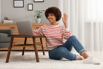 Canvas Print - Beautiful young woman having video chat via laptop and saying hello at wooden coffee table in room