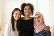 © fizkes - Three cheerful multicultural office colleague friends standing together, hugging, laughing, looking at camera with toothy smile. Diverse multiethnic coworker women team portrait