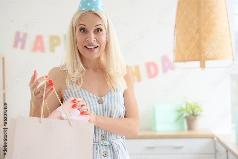 Mature woman taking birthday gift from bag in kitchen