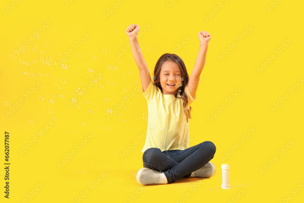 Happy little girl and soap bubbles on yellow background