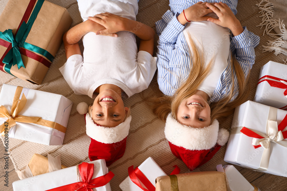 Little children with Christmas presents lying on carpet, top view