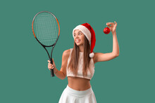Sporty Young Woman In Santa Hat With Tennis Racket And Christmas Ball On Green Background
