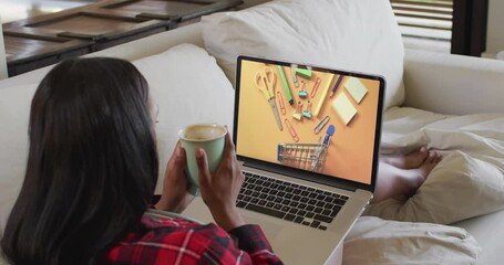 Wall Mural - Biracial woman using laptop on couch at home online shopping for stationery, slow motion